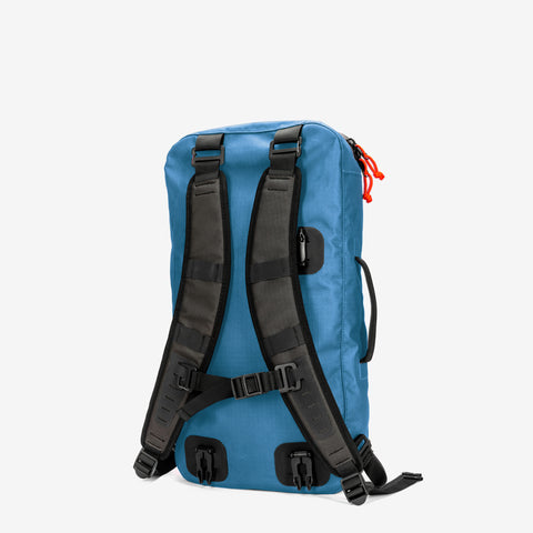 A stylish blue backpack with black shoulder straps, an adjustable chest strap, and red zipper pulls from Cancha's Padel & Pickleball Bundle is viewed from the back. It's made to accommodate modular accessories and includes a convenient detachable wet-dry bag.