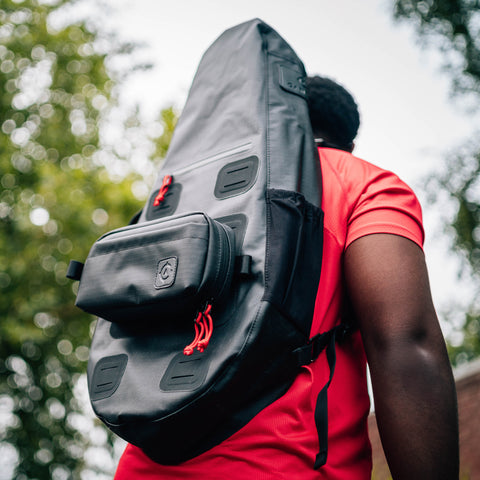 A person in a red shirt carries a Cancha Sling Bag outdoors, showcasing its versatile design and travel functionality.