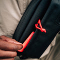 A person is placing a red card with the text "monzo" into the small, weather-resistant pocket of a black Cancha Sling Bag.