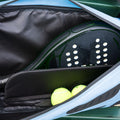 A close-up of an open Cancha Padel & Pickleball Bundle bag containing a green padel racket and two yellow tennis balls, featuring modular accessories for added convenience.