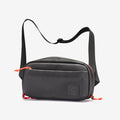 The Cancha Sling Bag is a compact black crossbody bag with red zipper pulls and an adjustable strap. It features an adaptable design and weather-resistant pockets, displayed against a white background.